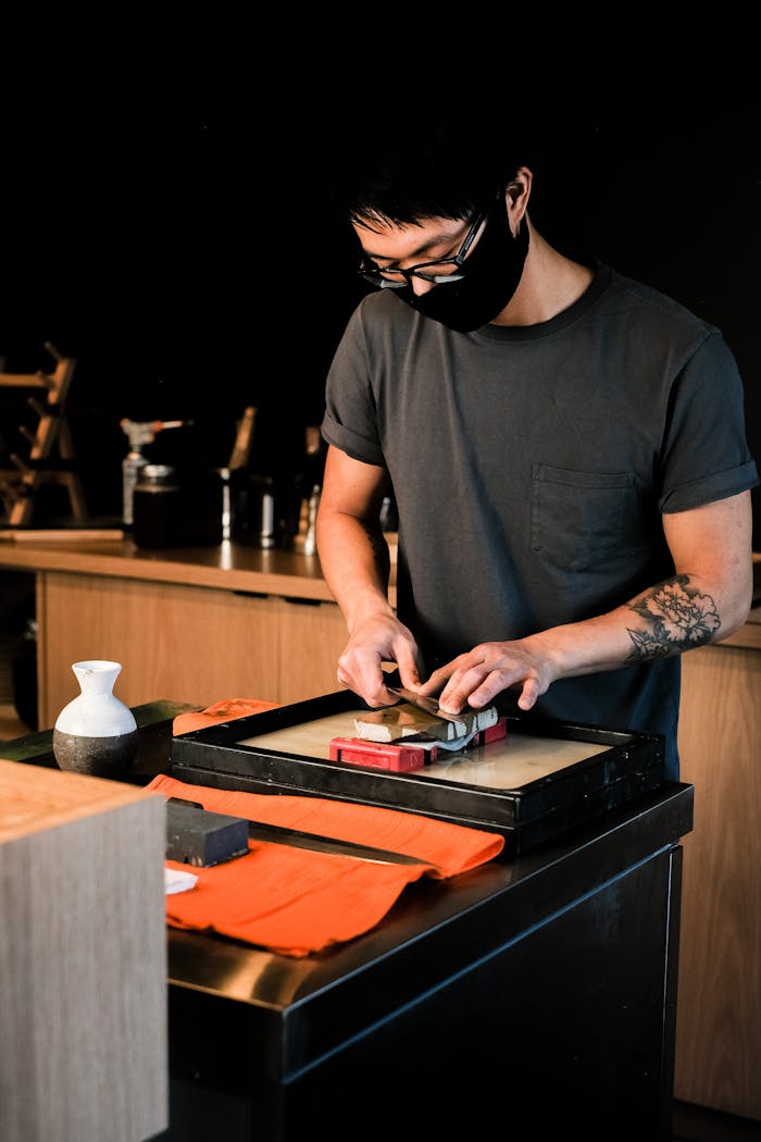 Accueil Asian chef sharpening a knife indoors using a whetstone in a Japanese restaurant setting.