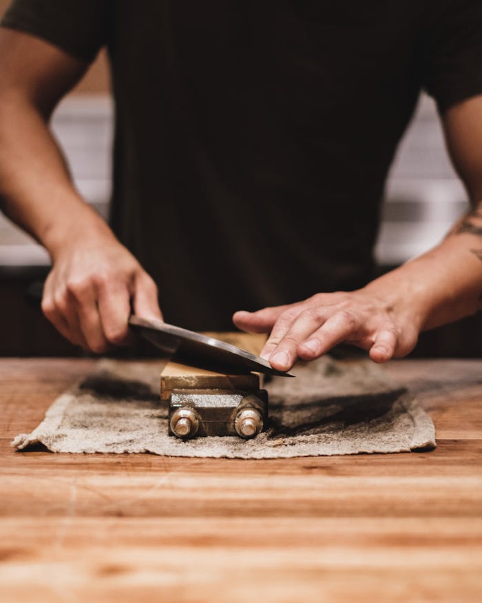 man-sharpening-a-knife-9424957 A person sharpening a knife on a whetstone in an indoor setting. Focus on hands and technique.