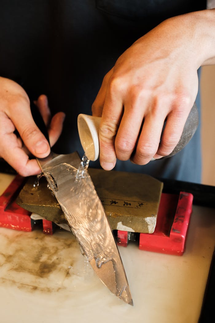 Accueil Close-up of hands sharpening a knife using water and a whetstone.