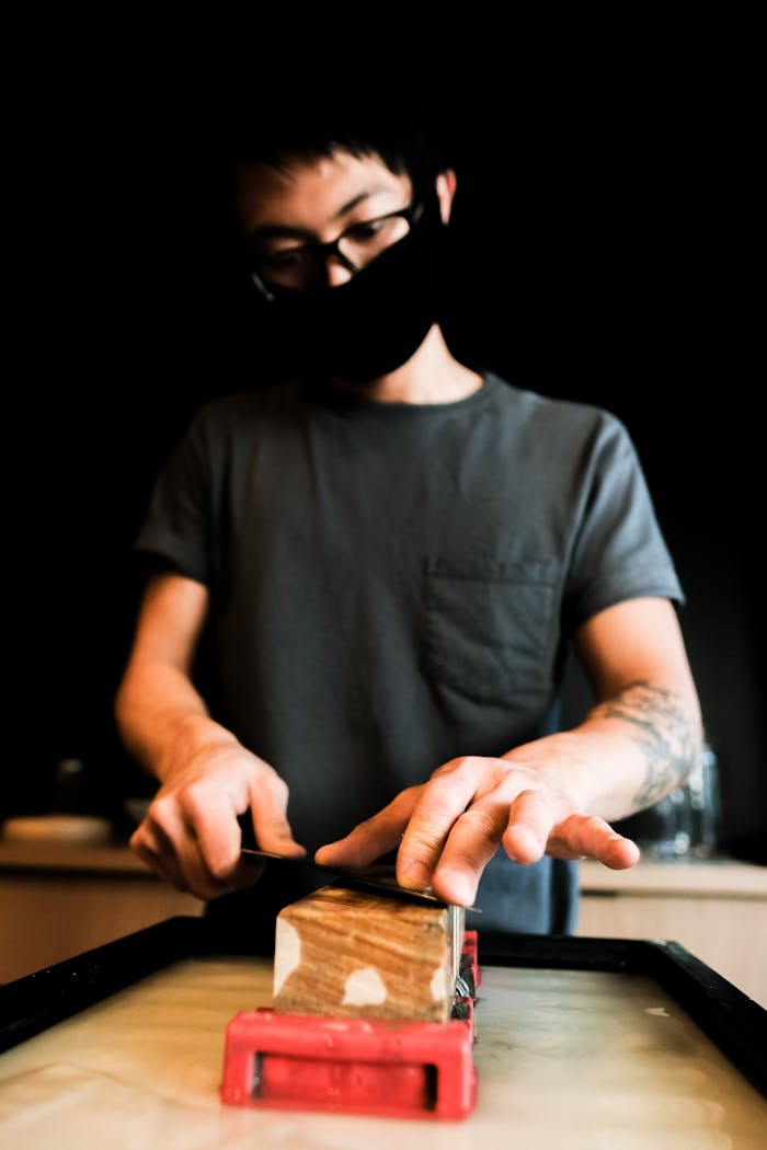 Accueil Close-up of a person sharpening a knife on a whetstone indoors, focusing on hands.